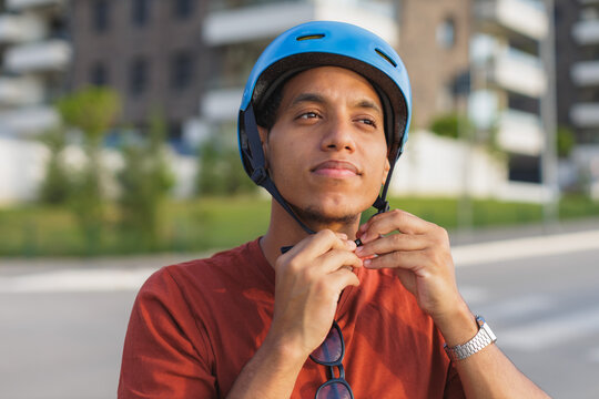 portrait of a young man putting on a blue helmet while preparing to ride a bicycle in the city