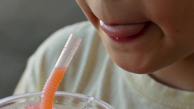 Child drinking red slushie through straw close up