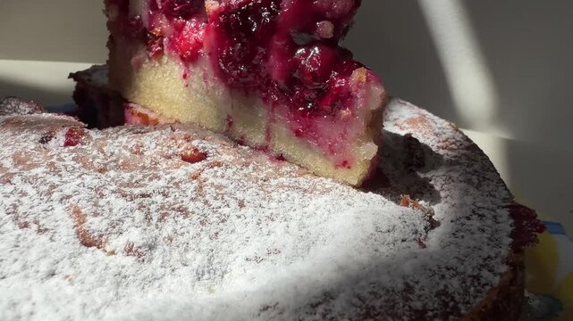 A homemade cherry sponge cake is shown whole, dusted with powdered sugar, and sliced to reveal its fruit-filled interior. The golden crumb and juicy cherries highlight a rustic dessert presented.