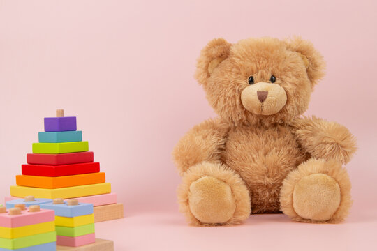 Colorful toys for children. Brown teddy bear and wooden toys on pastel pink background