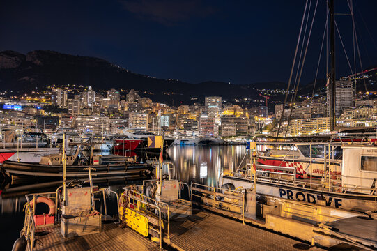 MONACO - JUNE 20, 2026: Modern luxury superyacht with underwater blue LED lights docked at Port Hercule harbour at night with Monte Carlo skyline in background.