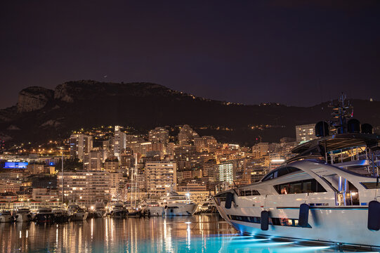 MONACO - JUNE 20, 2026: Modern luxury superyacht with underwater blue LED lights docked at Port Hercule harbour at night with Monte Carlo skyline in background.