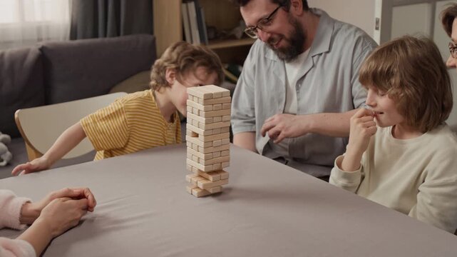 Caucasian family playing wooden block game at home, father watching sons carefully placing block on tower. Video for family bonding, board games, and indoor recreation marketing