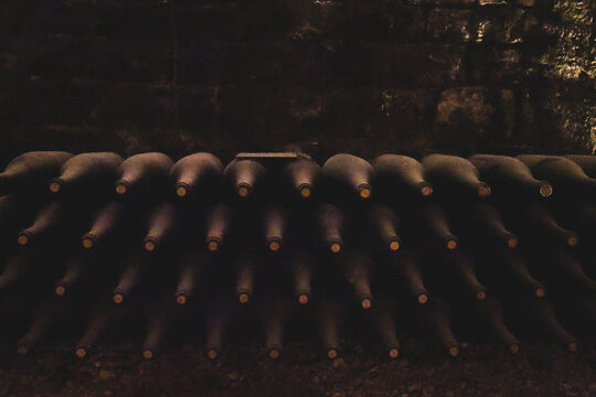 Rows of aging wine bottles rest horizontally in a dark Burgundy cellar, creating a minimalist pattern of glass and shadow that reflects the patience of traditional French winemaking.