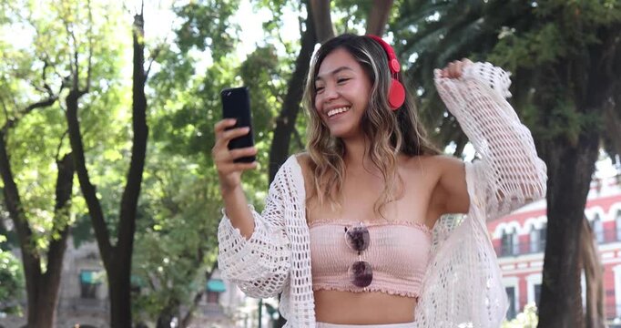 young latina woman using headphones and listening music in public park in Mexico Latin America