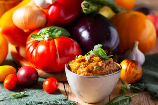 Eggplant caviar in a glass jar and vegetables on a wooden background.