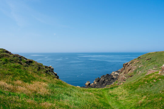 This scenic coastline view is Ramore Head in Portrush, Northern Ireland, featuring dramatic rock formations and the nearby Atlantic Ocean.