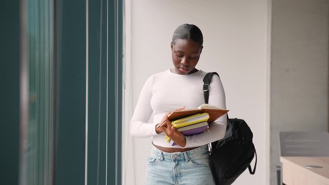 African american female student checking notes in a university hallway
