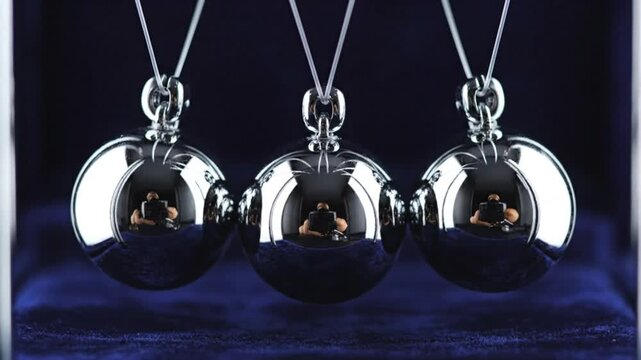 Newton's cradle demonstrates energy transfer with perfectly reflective chrome spheres suspended from strings inside a velvet case