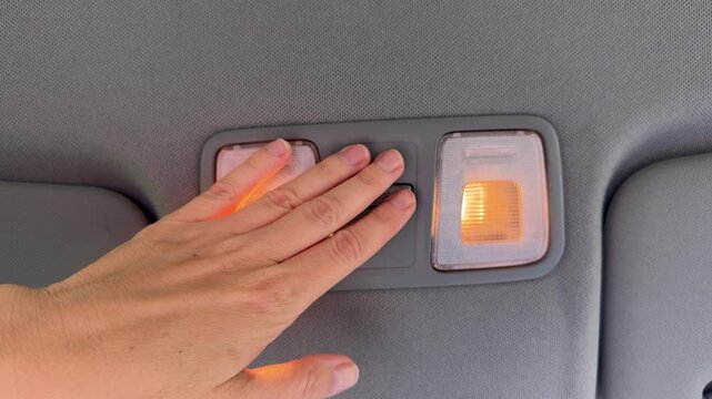 Hand pressing car dome light switch labeled door off on gray ceiling console with illuminated interior lights, automotive interior detail.