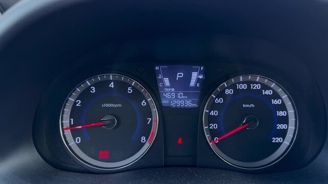  Close-up of car dashboard instrument cluster with speedometer, tachometer, digital display showing high mileage, parked in gear P with brake warning light.