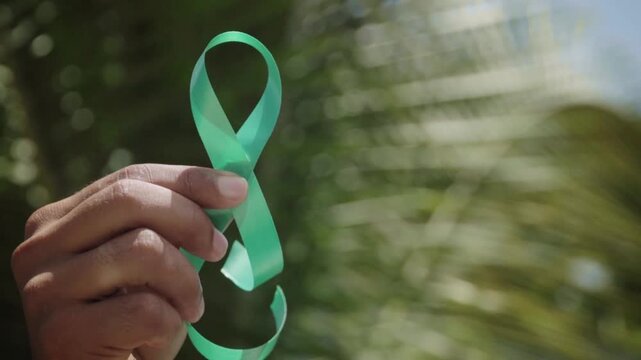 Hand holding green ribbon for mental health awareness