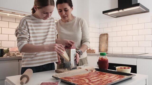 Mom And Daughter In The Kitchen Cooking Homemade Pizza And Shredding Parmesan Cheese For The Topping