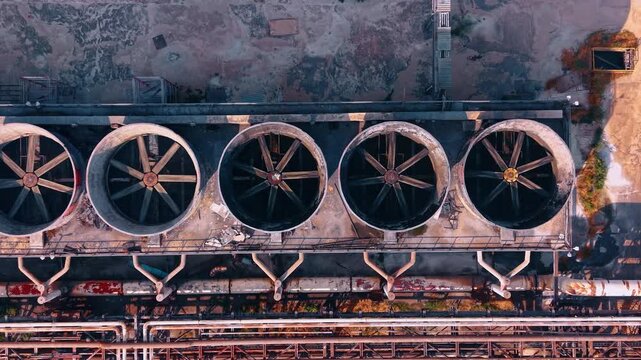 Towers with fans rotating for cooling. Footage over the heavy piping infrastructure of the plant.