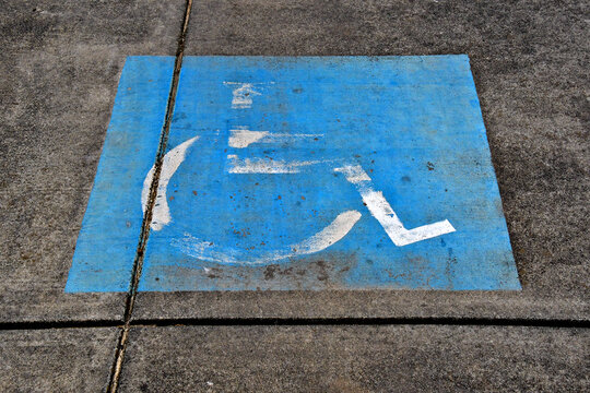 Well worn Faded International Symbol of Access with a stylized image of a person in a wheelchair on blue background 