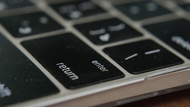 Close up of finger pressing return key on laptop keyboard with white and black keys