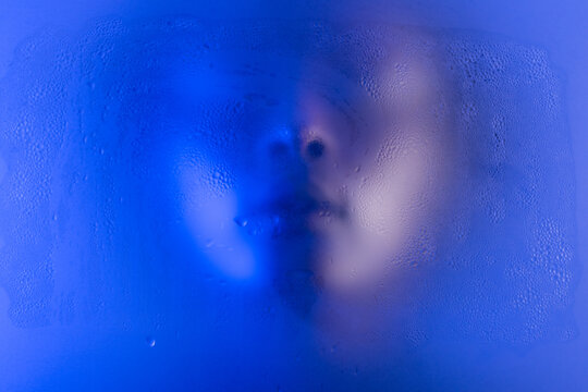 Anonymous black woman portrait behind the wet frost glass in blue light. 
