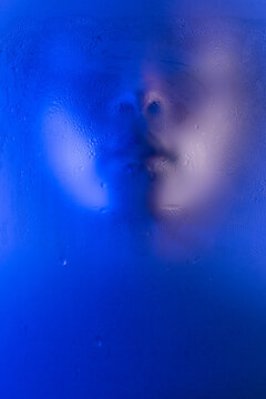 Portrait of young black woman behind wet frosted glass. Closeup of face with closed eyes. Anonymous beauty.
