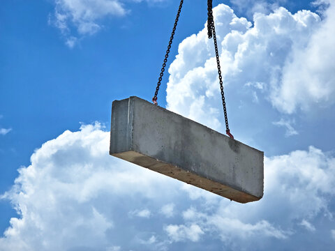 A concrete block suspended by heavy chains against a backdrop of a blue, cloudy sky.