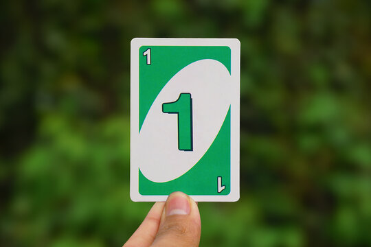 Hand Holding Green Number 1 UNO Card Against Blurred Background	