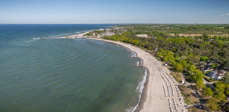 Baltic Sea coast line with a long sandy beach lined with traditional German hooded beach chairs, green coastal forest. Beach at Timmendorfer Strand and Niendorf in the L&uuml;beck Bay.