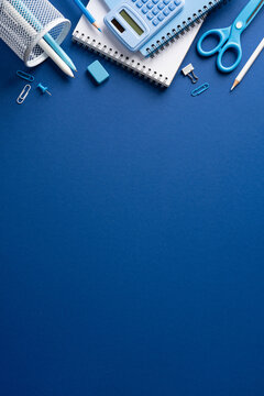 Back to school flat lay with blue stationery, notebook, calculator and scissors on paper on vertical dark blue backdrop with blank space