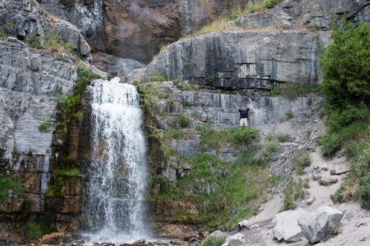 Man celebrates as reaches the waterfall after a long hike.  Enjoying a vacation in nature hiking to Stewart Falls near Sundance, Utah on Mount Timpanogos.  Celebrating an achievement.