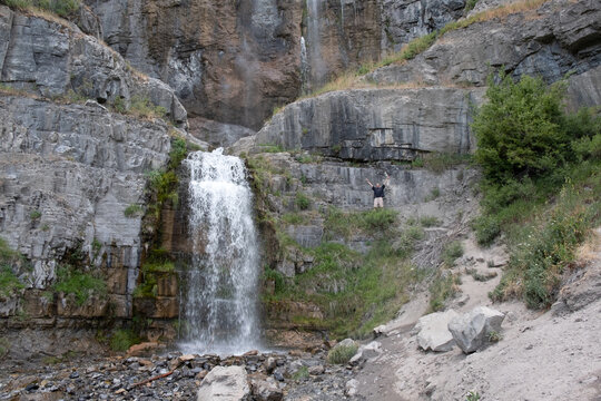 Happy a victorious, man reaches the waterfall at the end of the hike.  Man's arms outstretched over head to celebrate completing the hike to Stewart Falls, Utah.