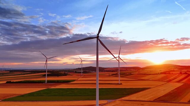 Wind turbine farm during colorful sunset. Warm orange light fills the sky over vast agricultural fields with multiple clean energy generators.