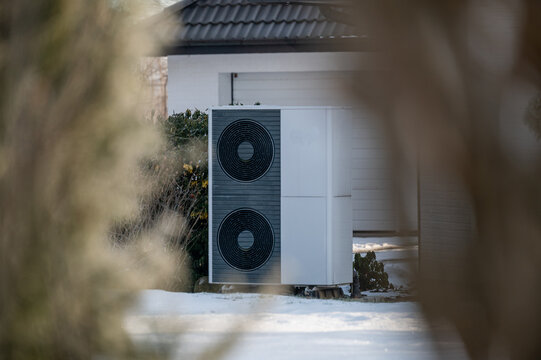 Air source heat pump outdoor unit in winter house backyard covered with snow for sustainable renewable heating.