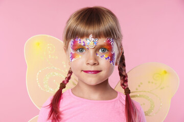 Fototapeta premium Little girl with beautiful face painting and fairy wings on pink background