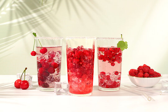 Modern still life with berry juice, raspberries, cherries, red currants, and ice on an elegant kitchen table, casting long, sharp shadows. The concept is a minimal detox diet, summer vitamin drinks,