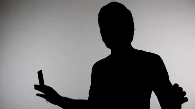 Anonymous silhouette of a person stands in front of a light source creating a shadow on the wall during a quiet moment in a studio