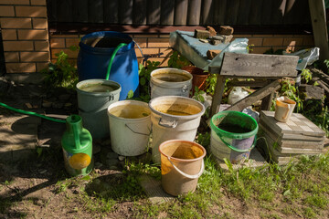 Naklejka premium Buckets and containers with different substances are arranged near a wooden structure in a garden area