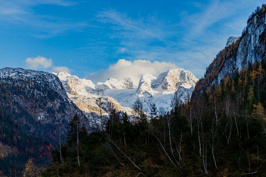 The colourful autumn scene of rocky Dachstein mountain range covered by snow surrounded by tall mountains and forested hills. Austria 
