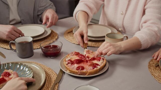 Caucasian young woman serving slices of strawberry pie to relatives during tea party. Ideal for food delivery services or bakery promotions