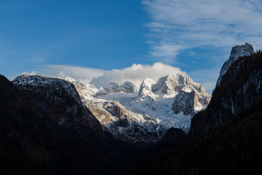Alpine view with snow-capped Dachstein Mountain surrounded by forested hills. Austria 