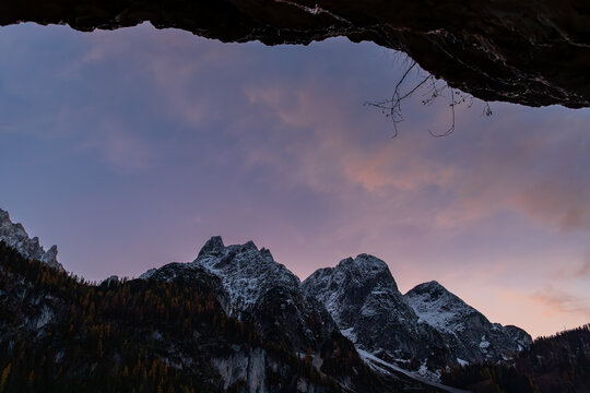 The view from inside a rocky cave on snow-capped mountain peaks under the purple twilight sky. Located in the Gosau Valley in Upper Austria.