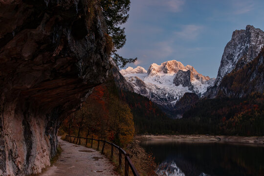 The walkway along Gosau lake (Upper Gosausee) surrounded by forested hills and snow-capped Dachstein mountains.Located in the Gosau Valley in Upper Austria.