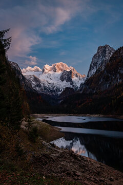 The evening scene of Gosau lake (Upper Gosausee) and snow-capped mountain peaks bathed in warm light of sunset. Located in the Gosau Valley in Upper Austria.