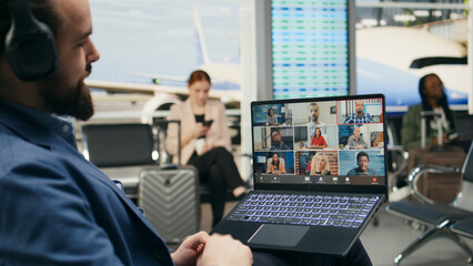 Naklejka premium Businessman attends a laptop video conference in an airport lounge, discussing work with associates and shareholders during business travel and global collaboration.