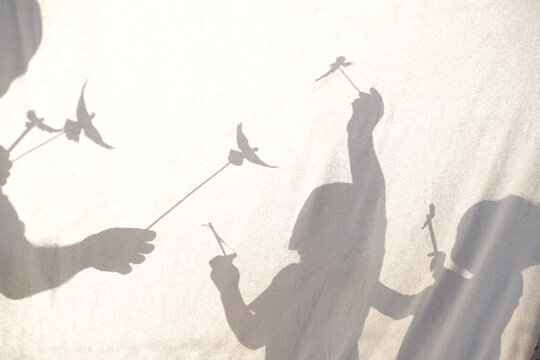Silhouette of an adult father and young kids playing behind a white sheet canvas. Conceptual light and shadow play capturing innocence, freedom, and sweet childhood dreams