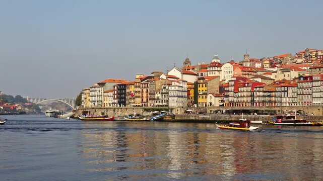 Colorful traditional houses of the ribeira district reflecting on the douro river in porto, portugal, with tourist boats sailing and the dom luis i bridge visible in the scenic background