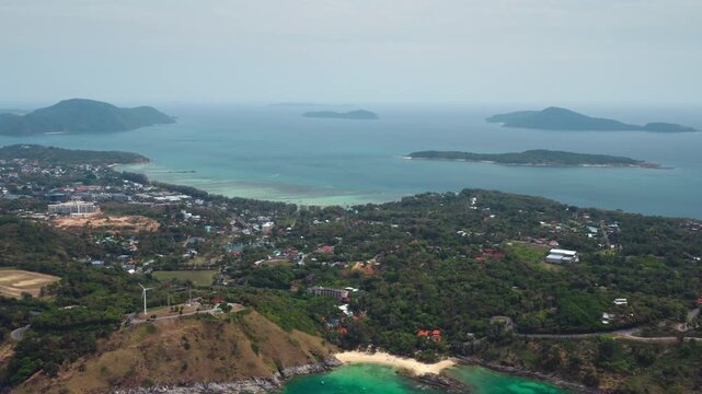 Phuket aerial landscape capturing the lush green coastline of a tropical island with Nai Harn Beach, turquoise sea, and distant islands under a clear sky, a popular tropical destination. Drone footage