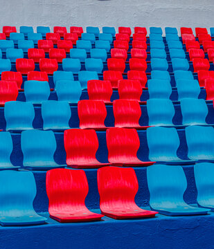 Repeating rows of bright blue and red empty seats forming a colorful abstract pattern.
