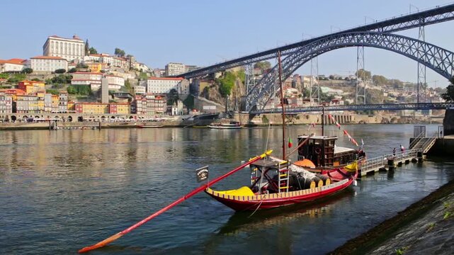 Scenic view of the famous dom luis i bridge and the historic ribeira district in porto, portugal, with a traditional rabelo boat moored on the douro river on a bright, sunny day