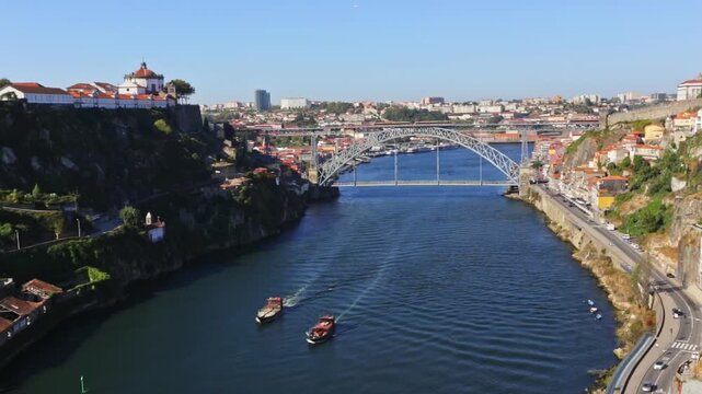 Scenic aerial view showing traditional rabelo boats sailing along the douro river with the historic dom luis i bridge and the vibrant ribeira district in the background on a sunny day