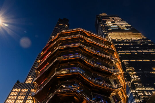 New York, NY - US - Jul 20, 2026 Low angle night view of the Vessel at Hudson Yards in New York City, glowing with warm lights against deep blue sky, surrounded by illuminated skyscrapers.