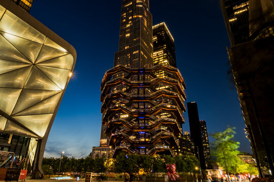New York, NY - US - Jul 20, 2026 Night view of the Vessel at Hudson Yards in New York City, glowing with warm lights against deep blue sky, framed by sleek skyscrapers and vibrant urban life.