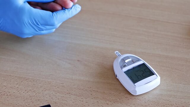 Medical professional in blue gloves checking a patient's blood glucose level using a lancing device to draw a blood drop from the finger and measuring it with a portable glucometer